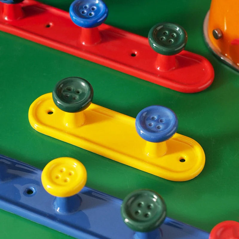 Close-up of colorful button ceramic wall hooks in red, yellow, and blue on a green surface. - RoomDen