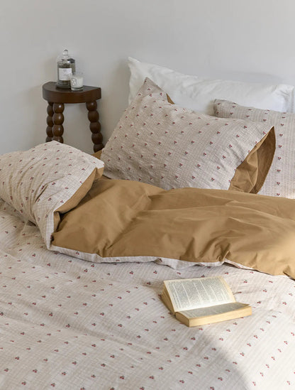 A cozy bedroom scene featuring the Textured Ditsy Cherry Washed Cotton Bedding Set with a wooden stool and candle nearby - RoomDen.