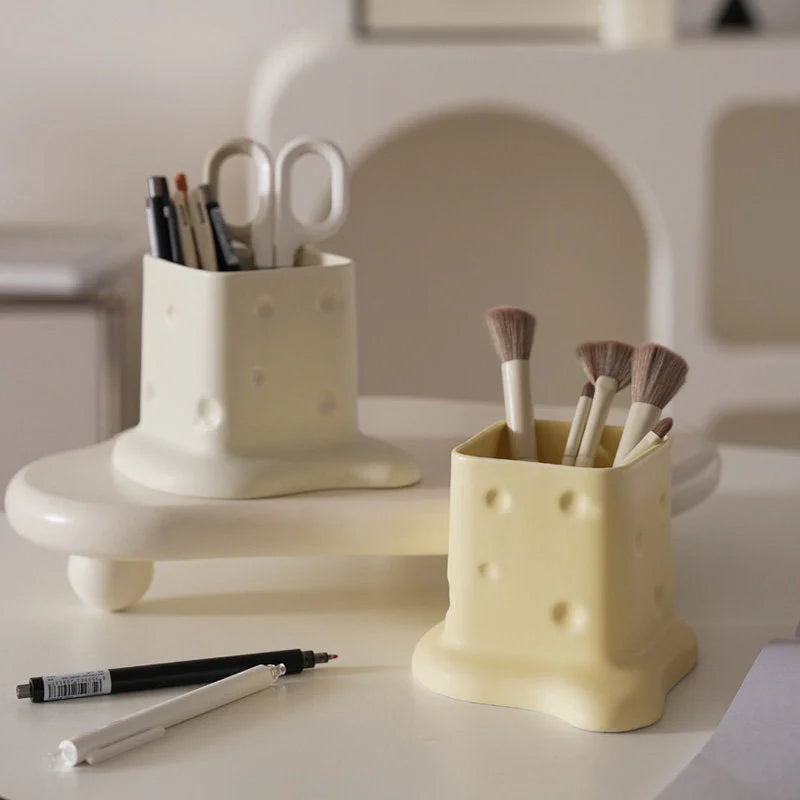 Two melting cheese organizers, one cream holding pens and one beige holding makeup brushes, on a white desk. - RoomDen