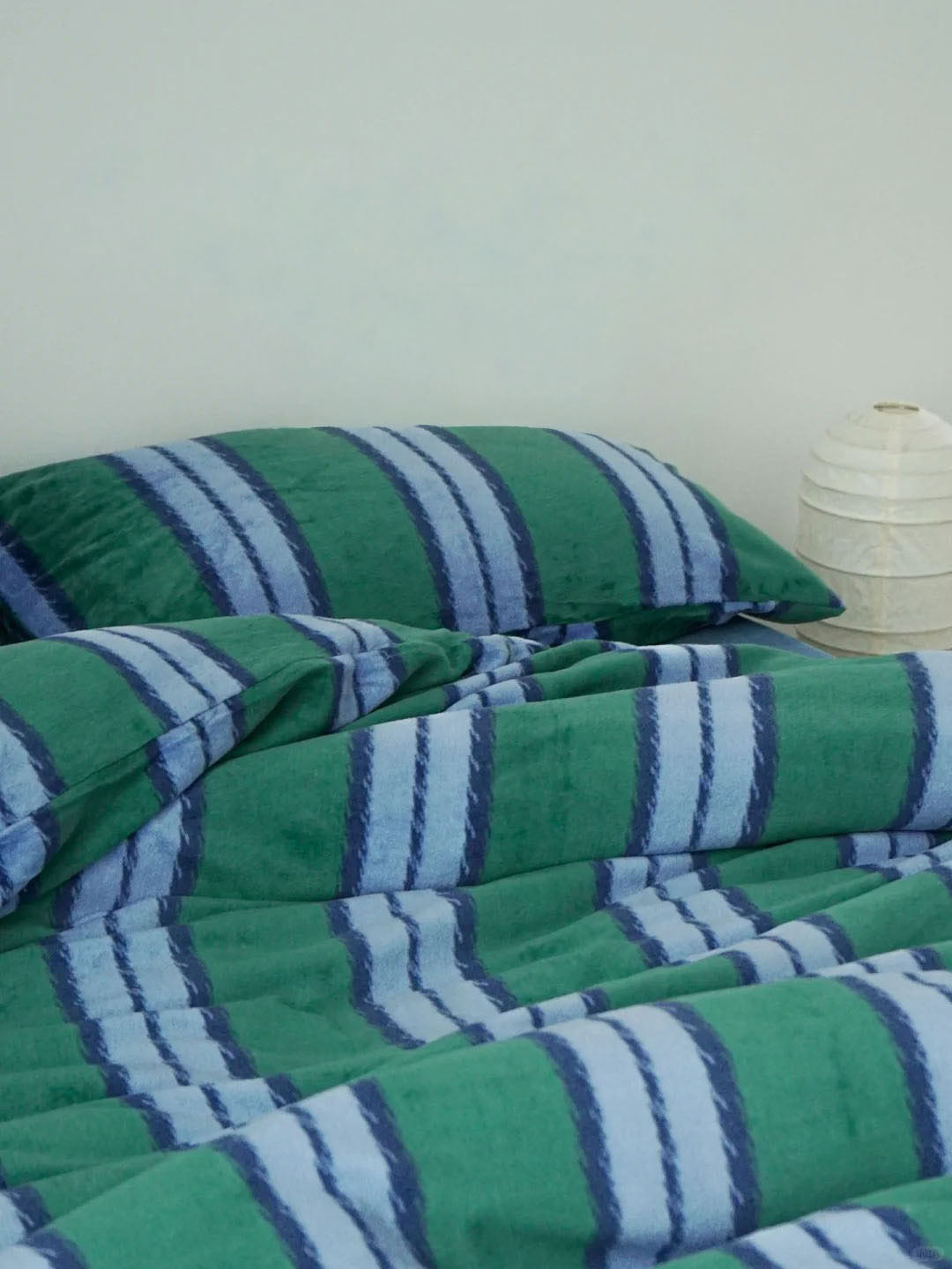 Minimalist bedroom featuring blue and green striped velvet bedding - RoomDen