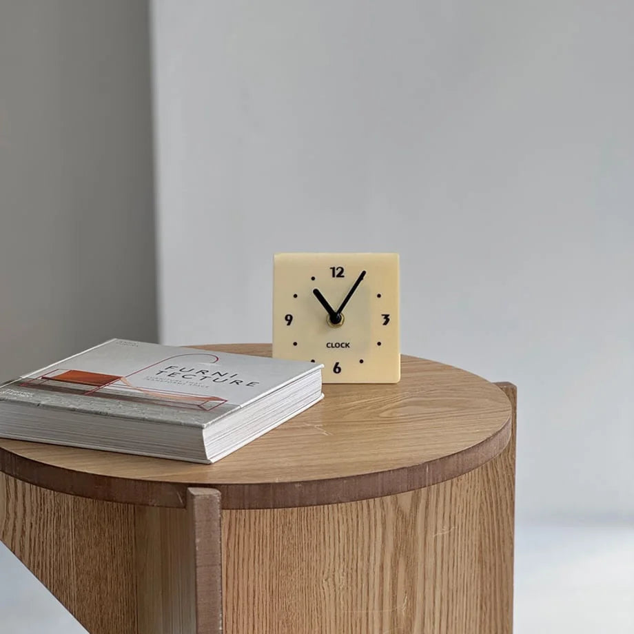 Cream Beige Sleek Minimalist Metal Table Clock on a light wood side table next to a book. - RoomDen