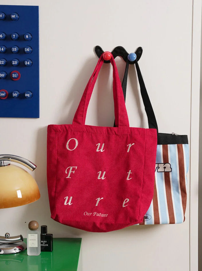 A red tote bag and a striped bag hanging from a black wavy wall hook with red and blue balls.