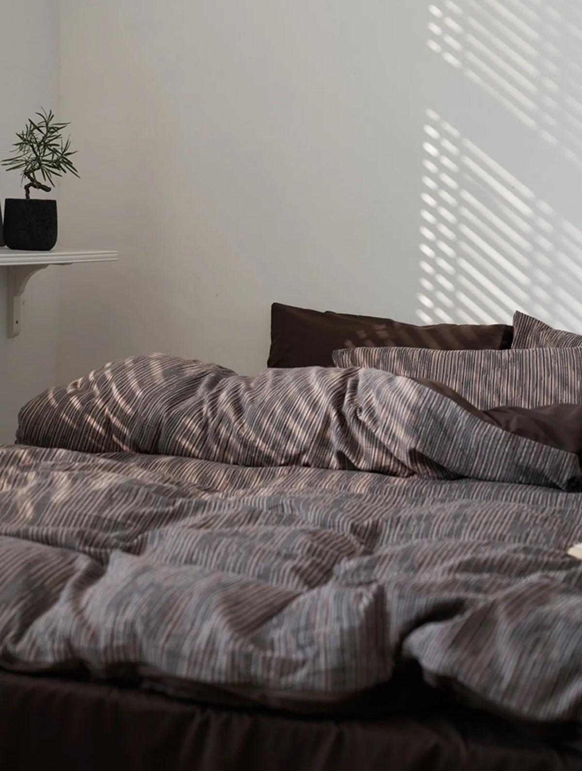 Wide shot of the Mocha Brown bedding in a minimalist room with a small plant on a shelf.