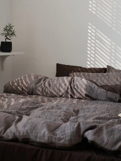 Wide shot of the Mocha Brown bedding in a minimalist room with a small plant on a shelf.