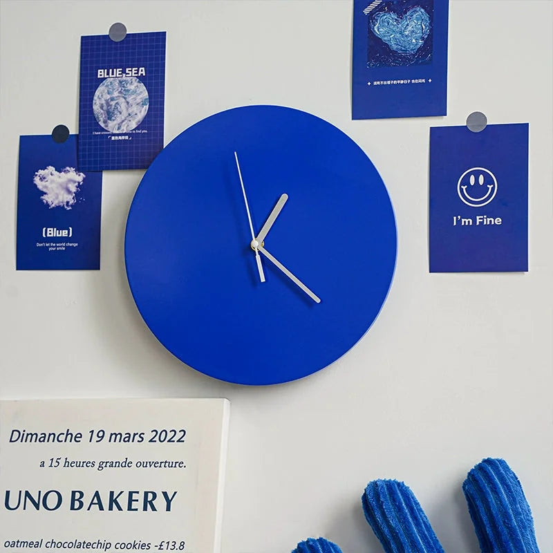 A vibrant Klein blue minimalist wall clock hanging on a white wall amidst blue-themed art prints, creating an Indie aesthetic gallery wall - RoomDen.