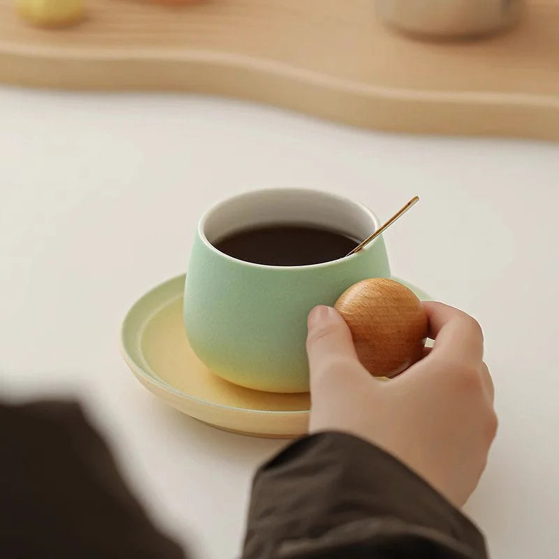 Close-up of a hand holding the Mint Green gradient ceramic mug with its unique spherical wooden handle. - RoomDen