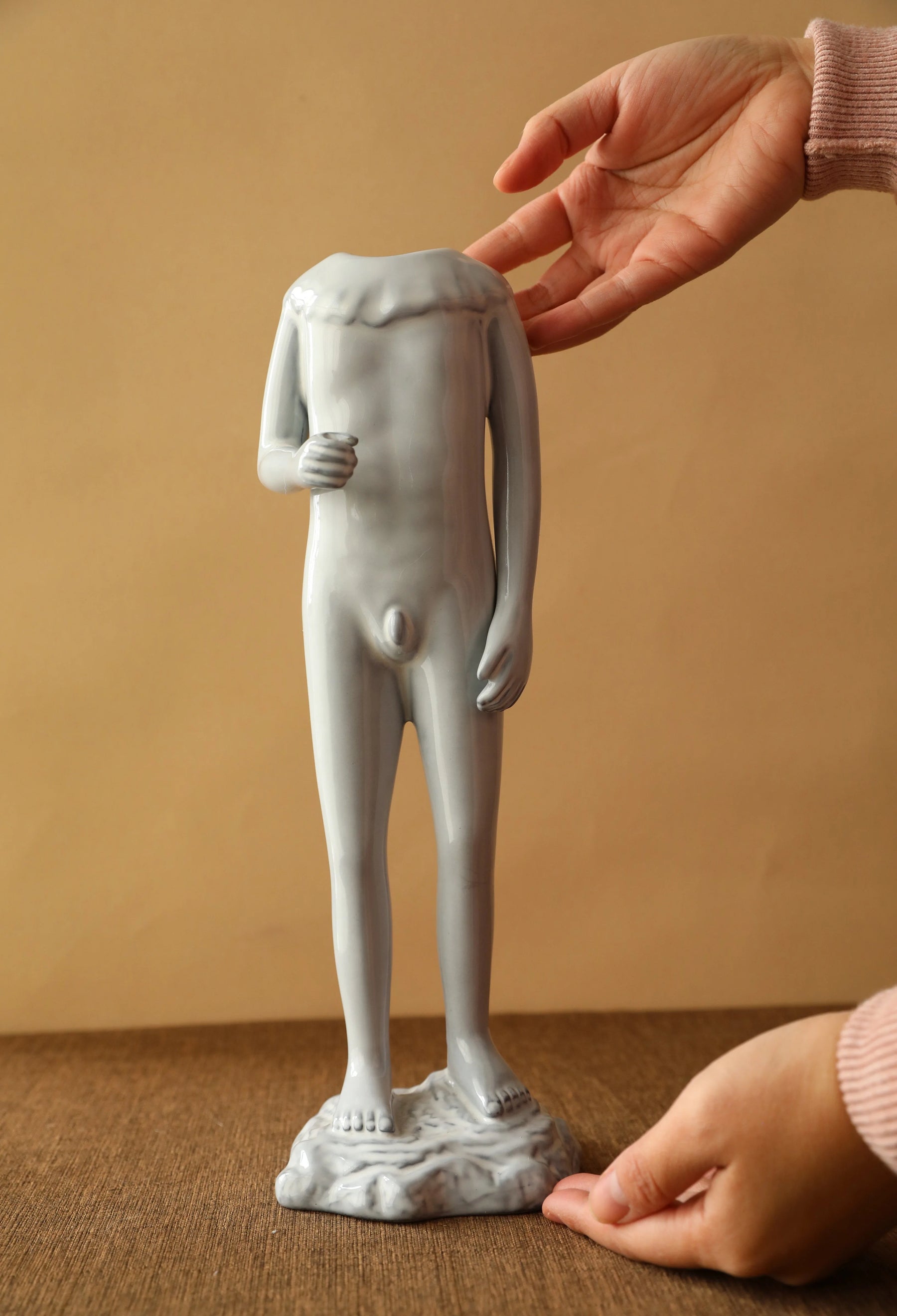 Hand positioning the male figure ceramic vase on a dark wood surface. - RoomDen