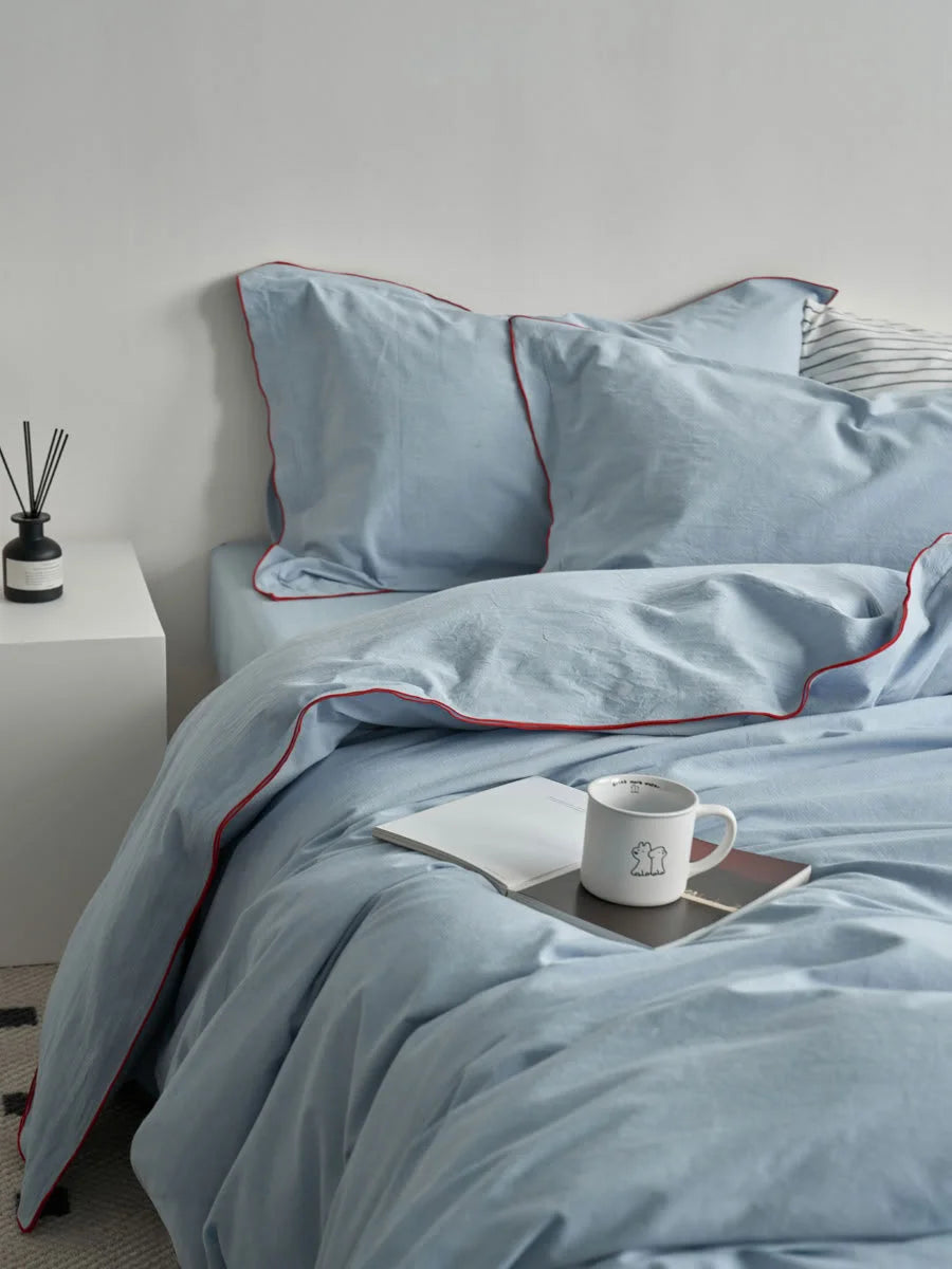 Sky blue washed cotton bedding set with red ruffle trim on a neatly made bed. - RoomDen