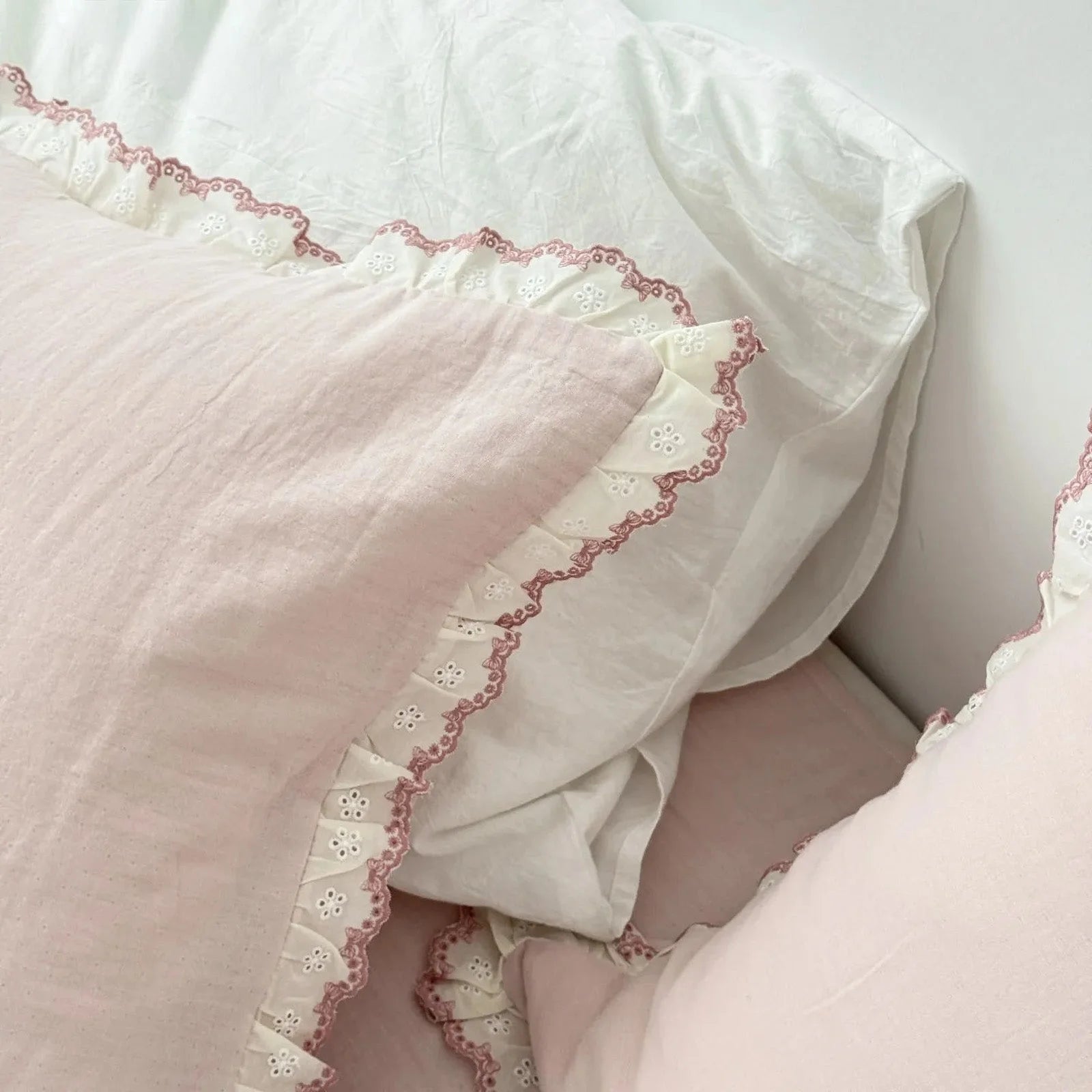 Tight shot of the delicate embroidered lace ruffle on the dusty rose pillowcase against a white pillow. - RoomDen