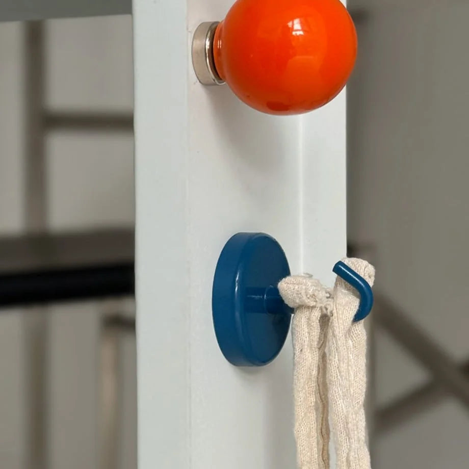 Orange and blue magnetic hooks on a white surface, one as a knob and one holding a cloth loop - RoomDen