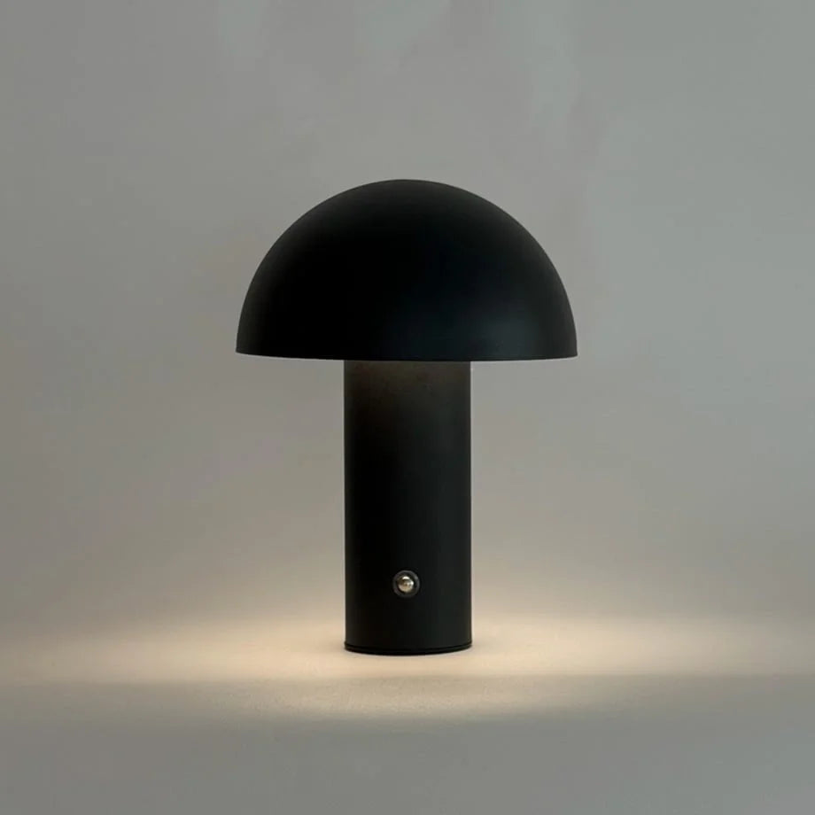 The black mushroom lamp emitting a soft, warm light, demonstrating its dimmable feature - RoomDen.