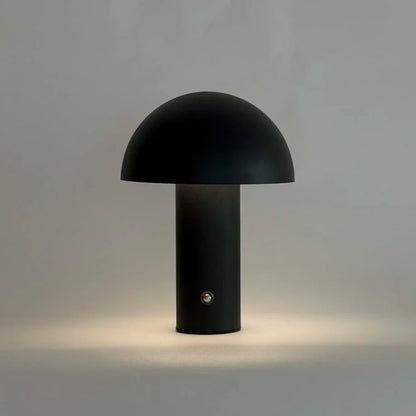 The black mushroom lamp emitting a soft, warm light, demonstrating its dimmable feature - RoomDen.