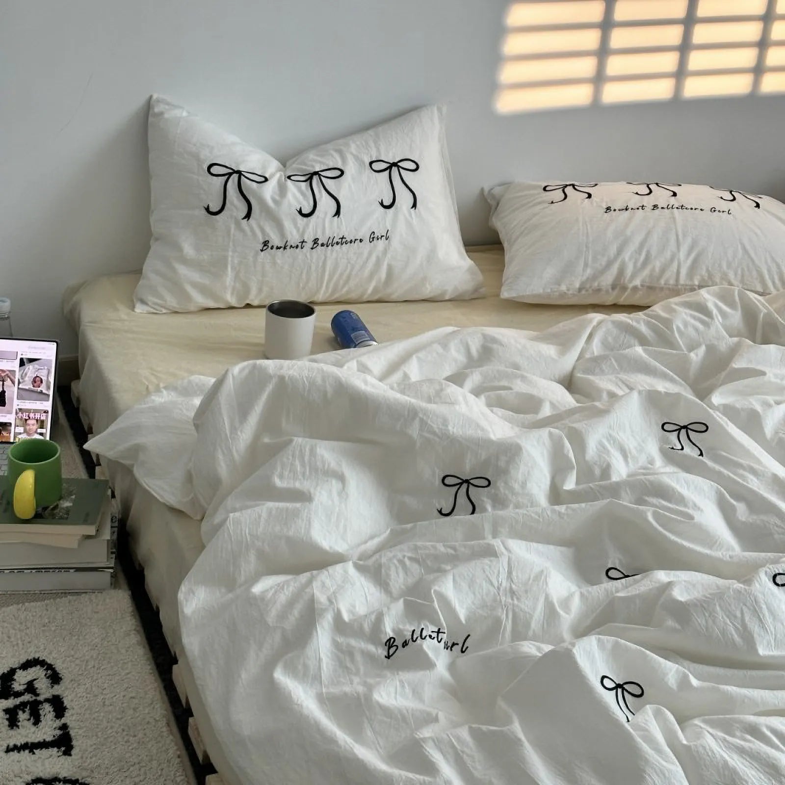 A bedroom scene with a white embroidered bowknot bedding set on a bed with a light-colored fitted sheet. - RoomDen
