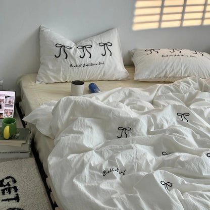 A bedroom scene with a white embroidered bowknot bedding set on a bed with a light-colored fitted sheet. - RoomDen