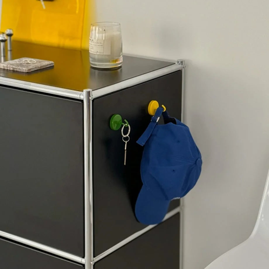 Green and yellow magnetic hooks on a black metal cabinet, holding a blue baseball cap and keys - RoomDen