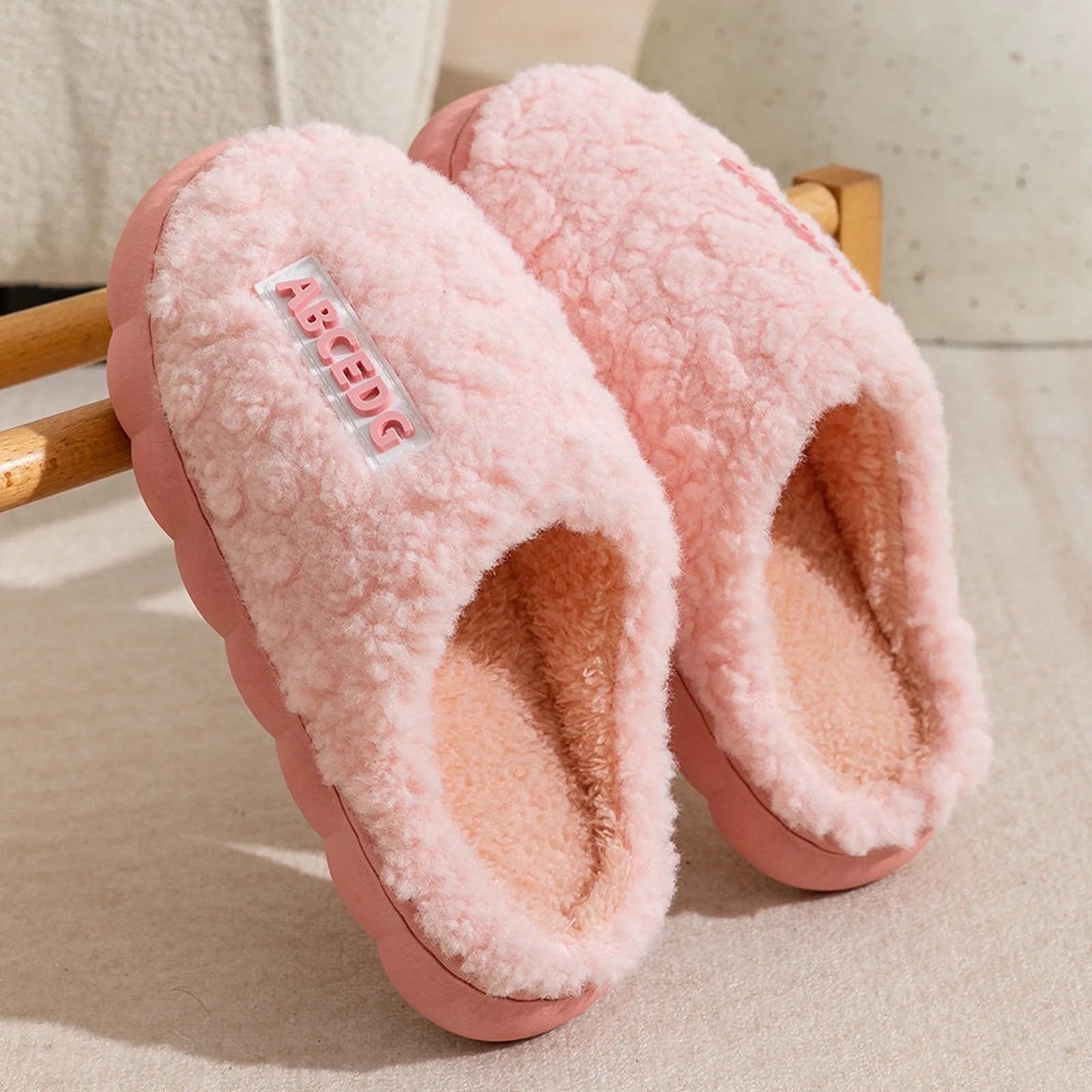 Monochrome Pink plush house slippers hanging on wooden rack - RoomDen