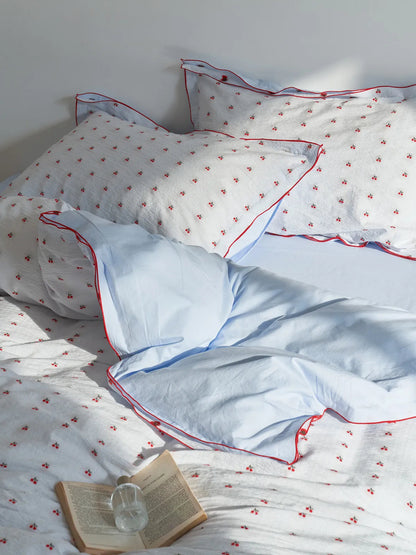 Sunlit view of the Ruffled Cherry Print Duvet Cover Set, showing the reversible solid blue side. - RoomDen