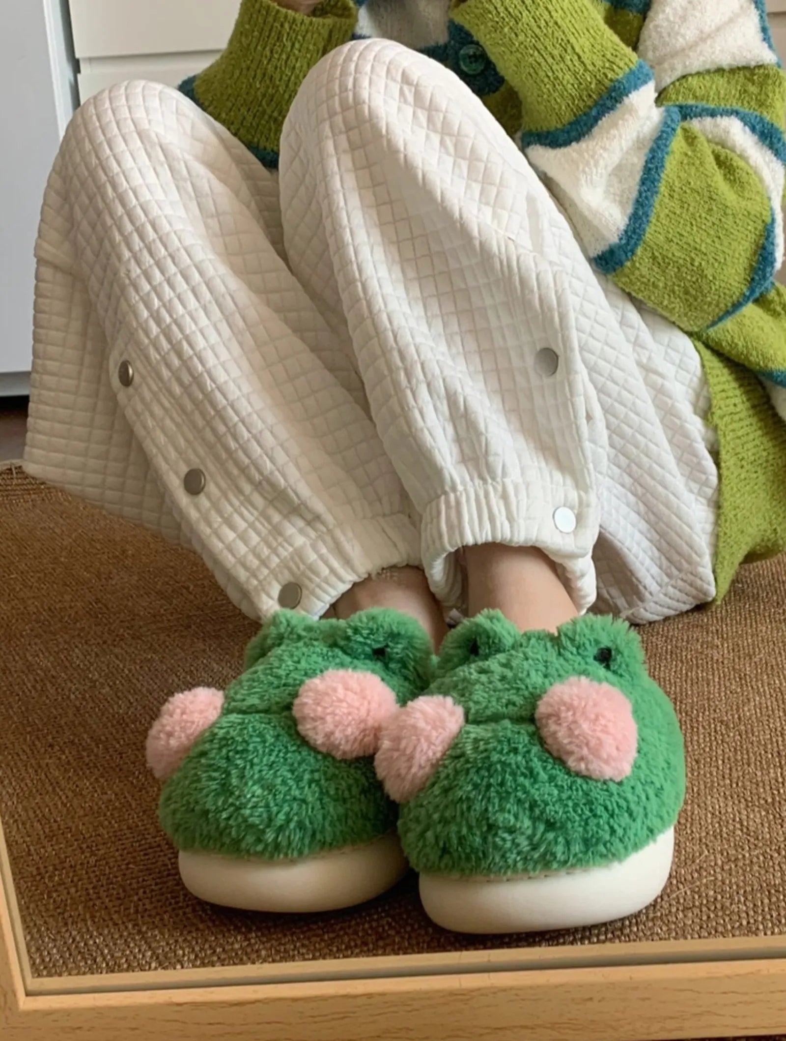 Person sitting wearing cute green frog slippers holding knees - RoomDen