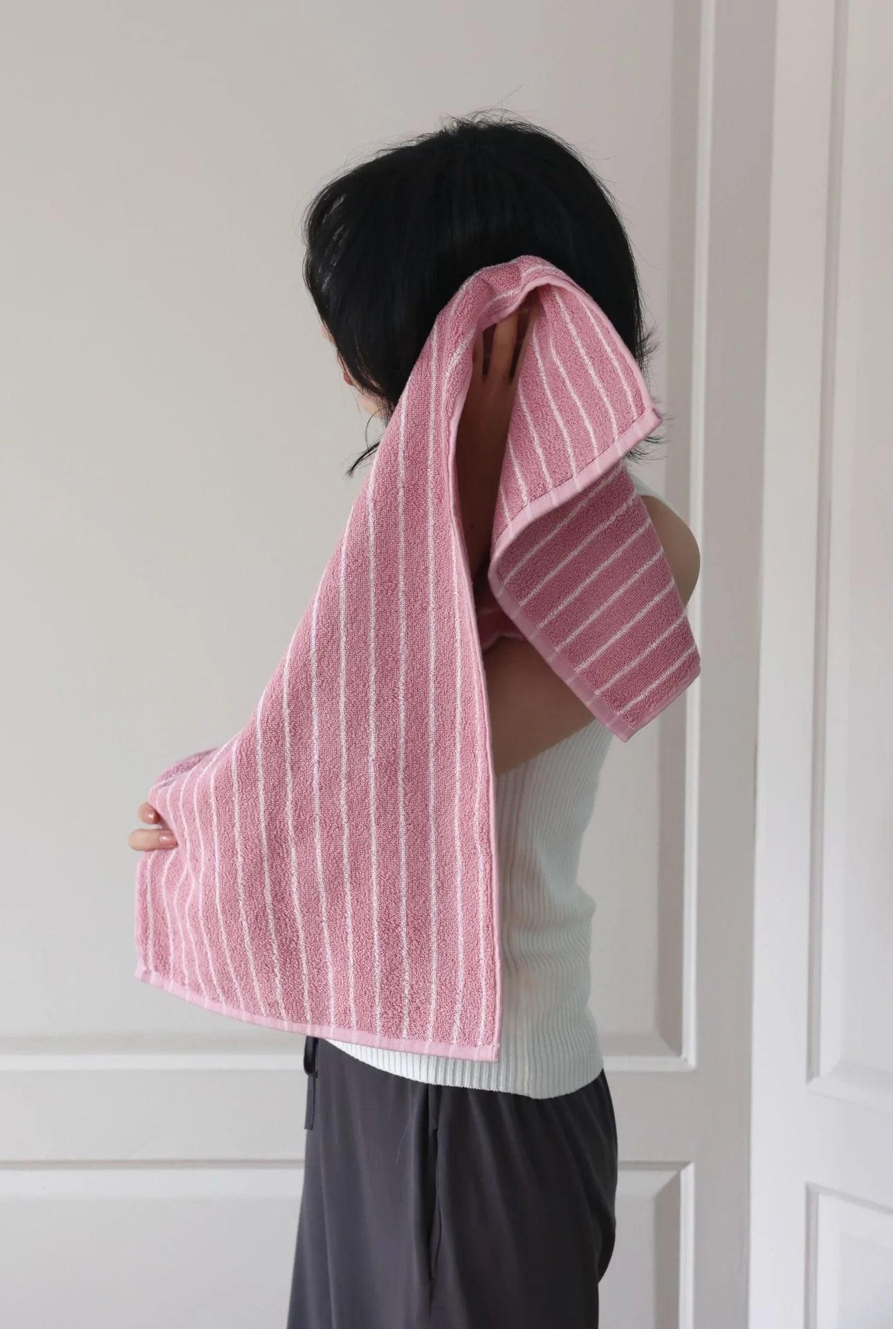 Close-up of a woman drying her neck and shoulders with a soft pink pinstripe cotton towel - RoomDen.