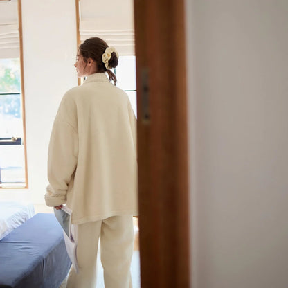Back view of the model wearing the oversized cream fleece pajama top, walking into a bedroom - RoomDen.