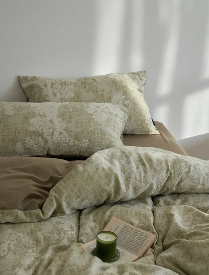 Close-up of a Jacquard Botanical Washed Cotton Bedding Set in sage green, showing the textured floral pattern and a green candle on a book - RoomDen.