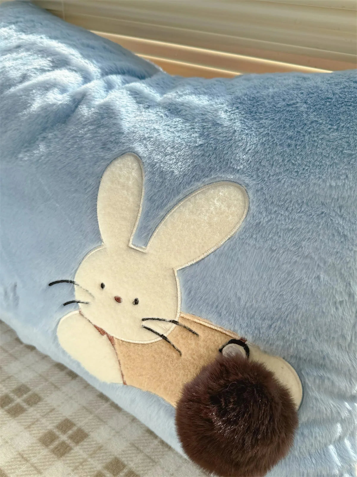 Detail shot of the embroidered bunny with a fluffy pom-pom tail on the blue pillowcase.