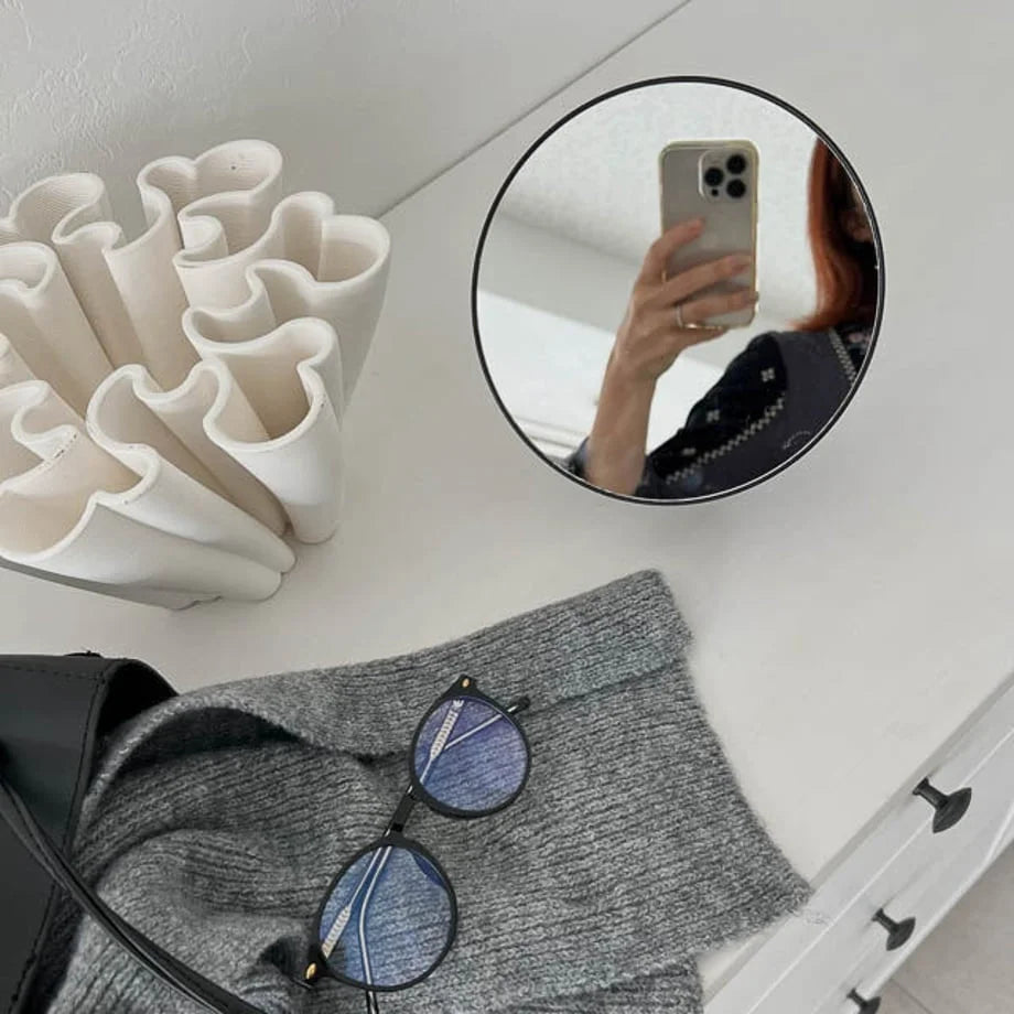 Reflection in the black minimalist makeup mirror showing a person taking a photo.