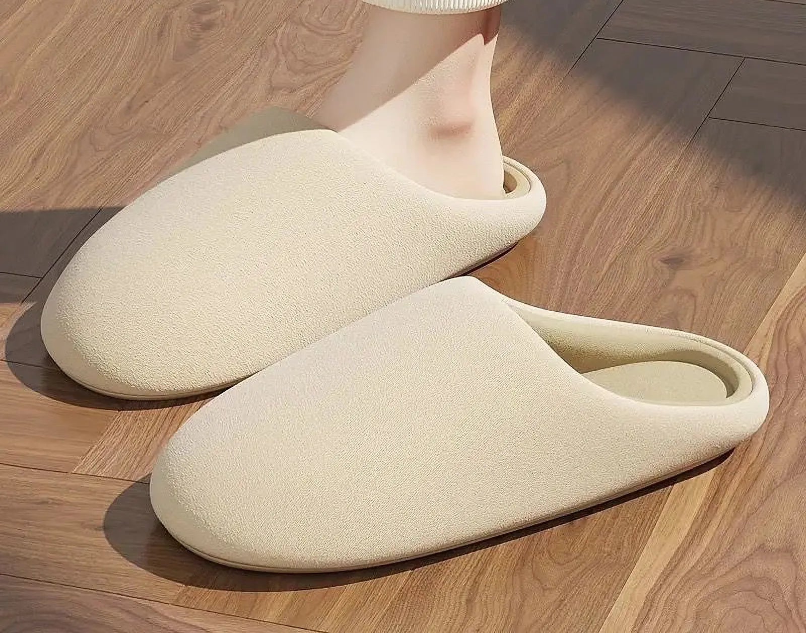 Beige plush slippers on feet on wooden floor - RoomDen
