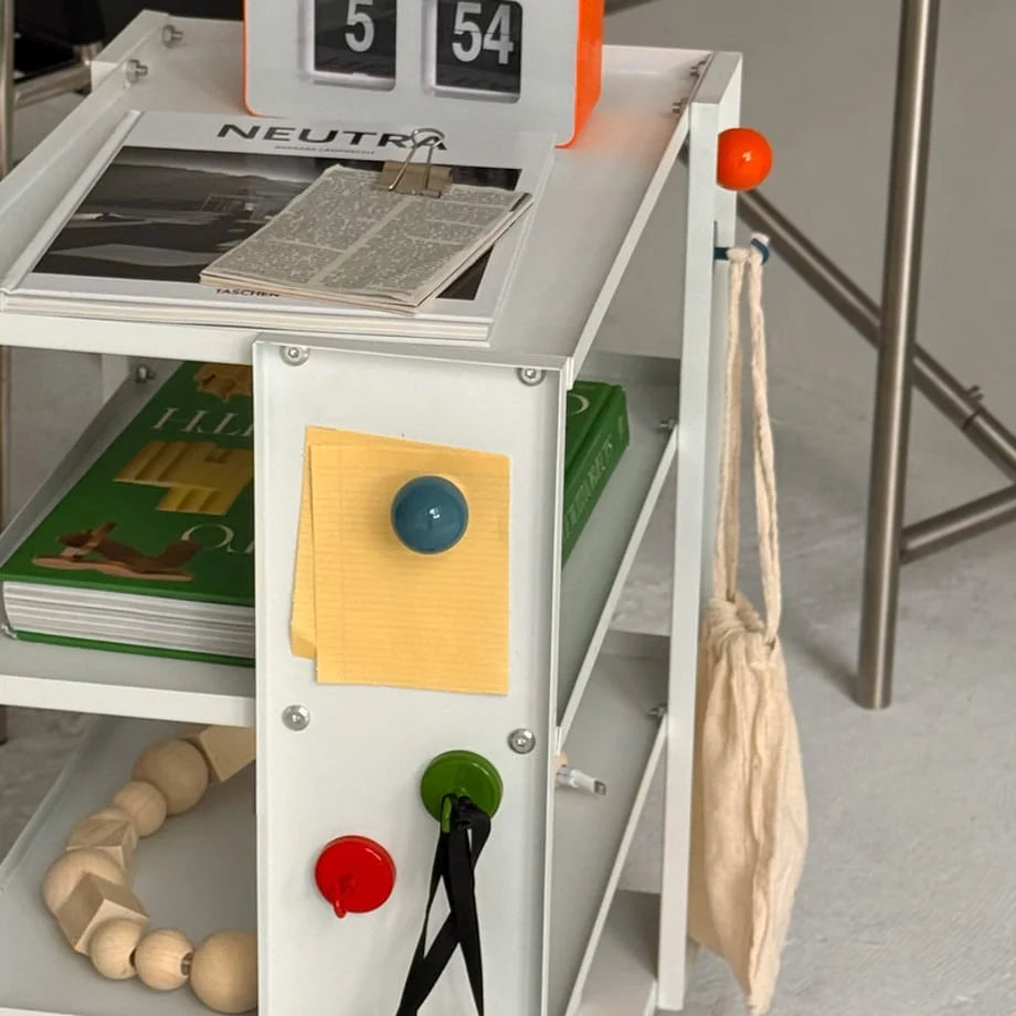 Red, green, and blue magnetic hooks used for bags and notes on a white shelf. - RoomDen