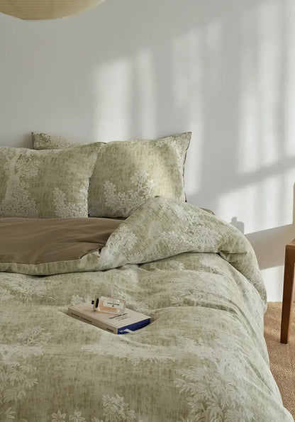 Full view of the sage green Jacquard Botanical Washed Cotton Bedding Set on a bed, styled with a perfume bottle on a book - RoomDen.