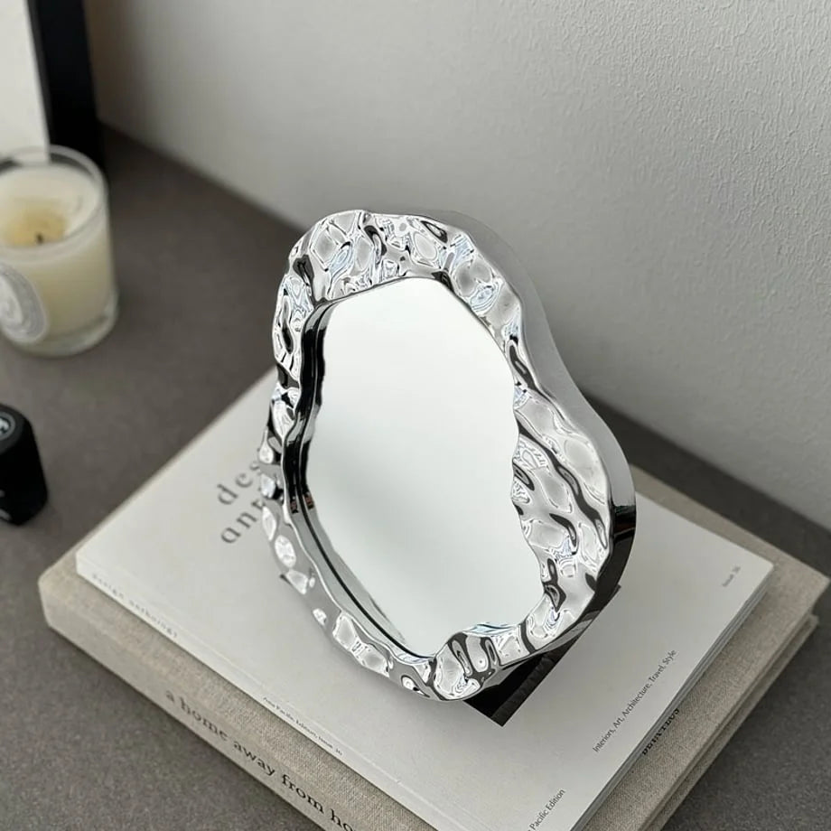 Angled shot of the asymmetrical chrome desktop mirror, showing its reflective, fluid frame - RoomDen