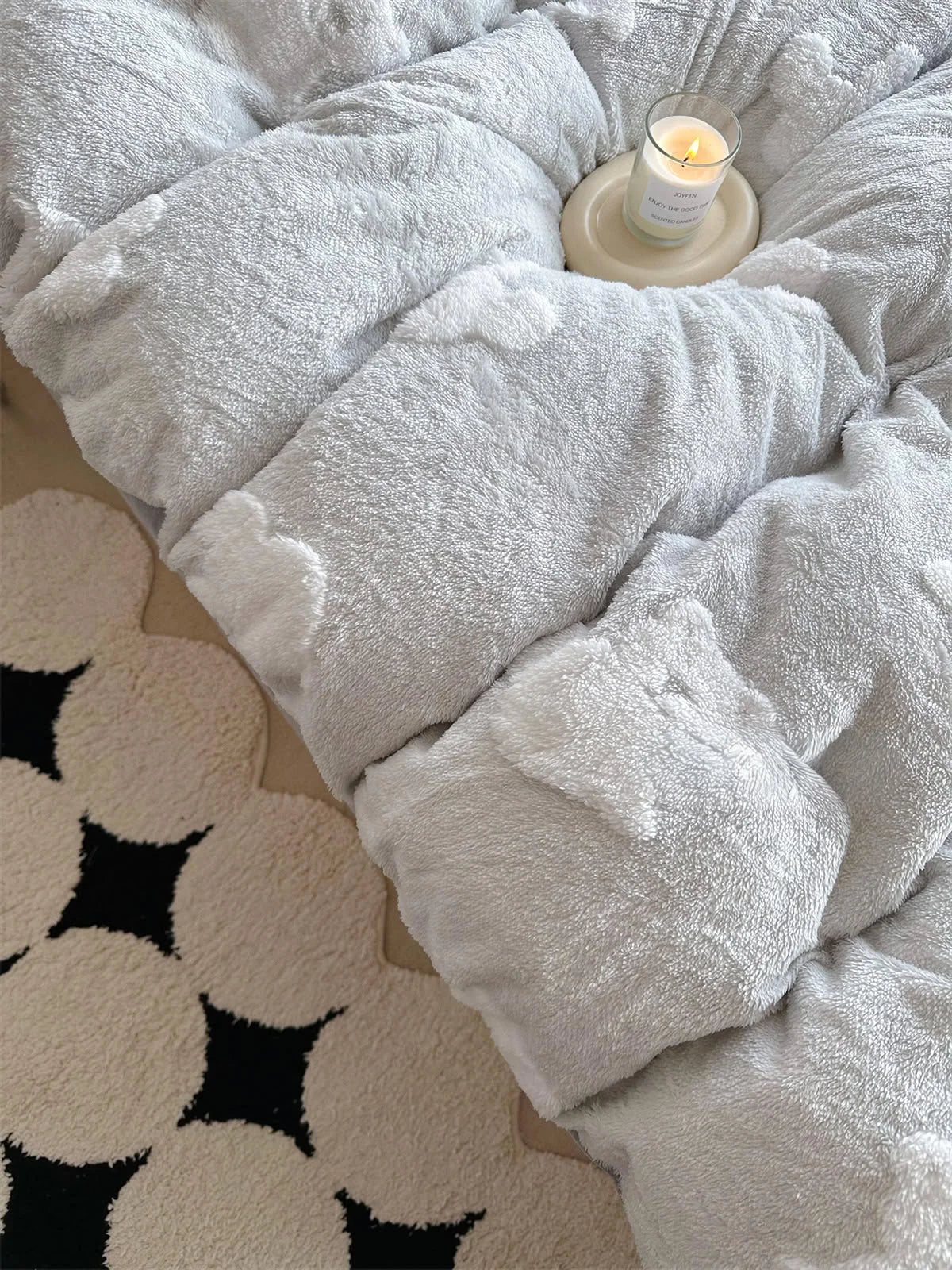 Top-down view highlighting the fluffy texture of the light grey bedding and a patterned rug below. - RoomDen