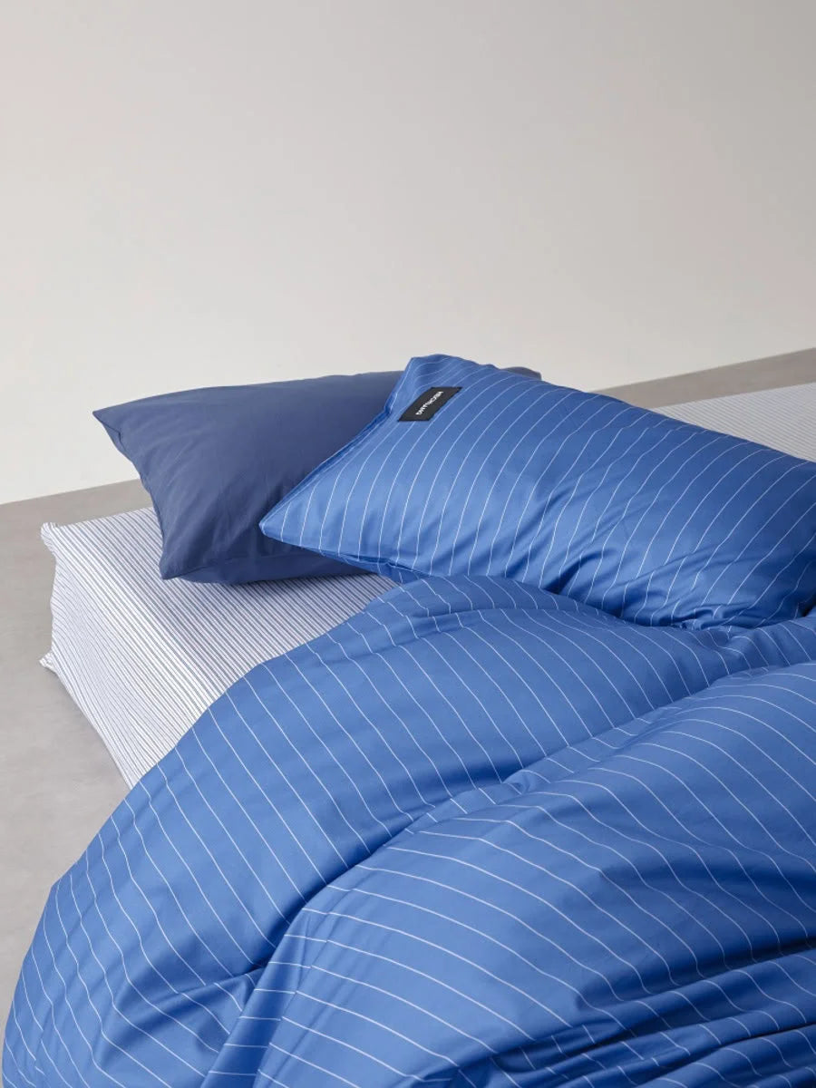 Close-up of the Denim Blue Pinstripe bedding set, highlighting the reversible solid blue pillowcase and striped sheet - RoomDen.