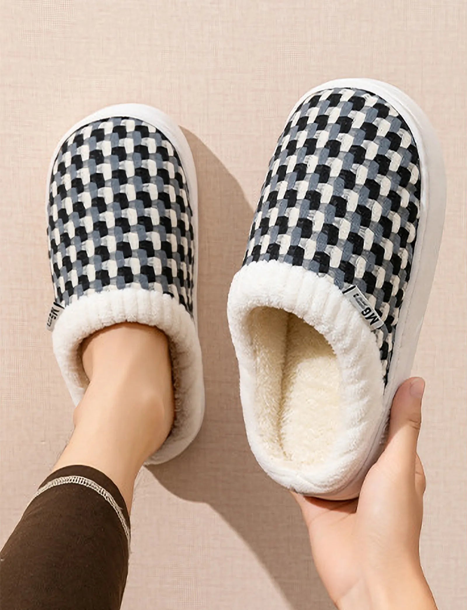 Top view of black and white woven gingham slippers held in hand