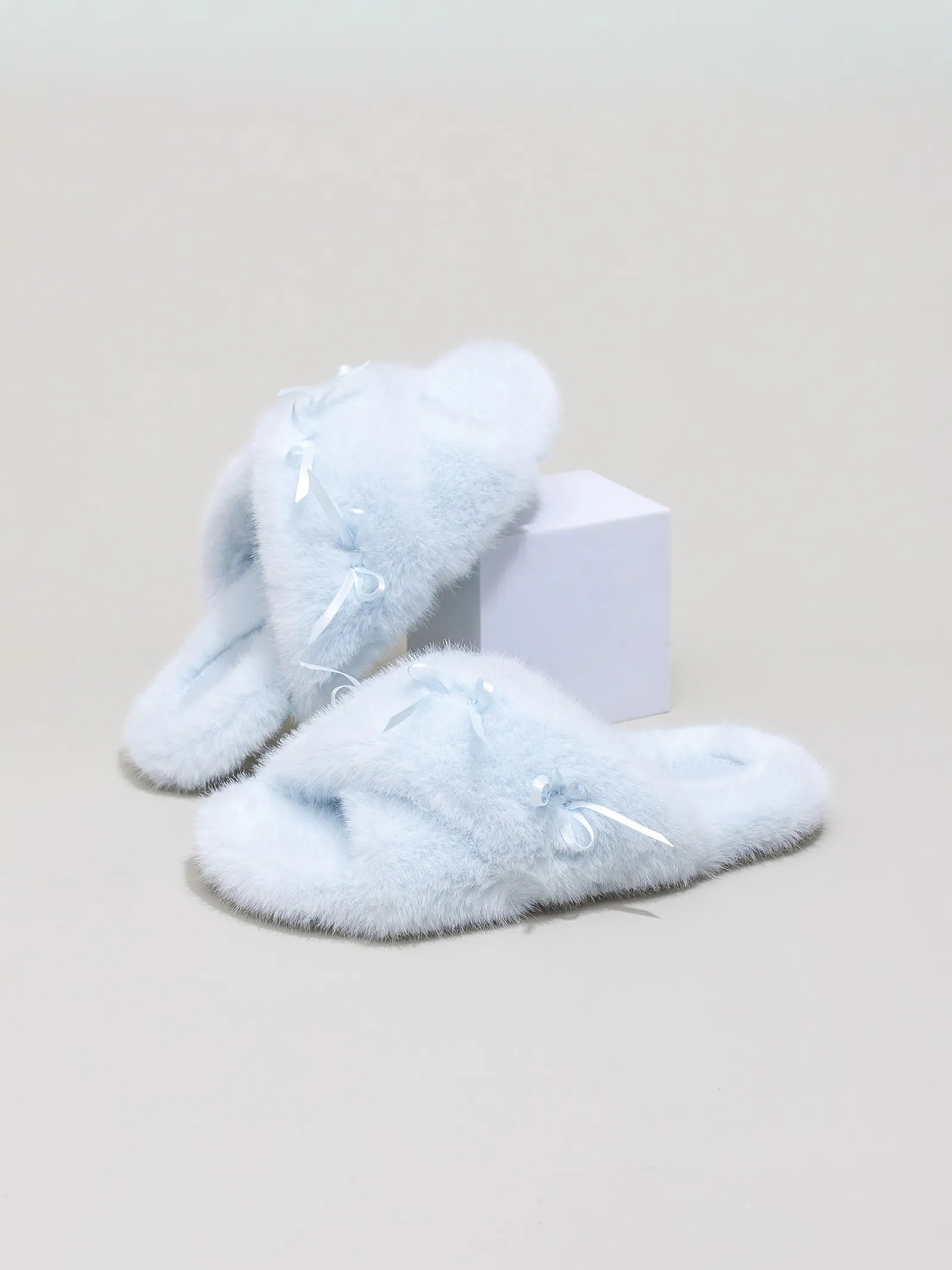 Pair of baby blue fluffy slides with bows on a white display block - RoomDen