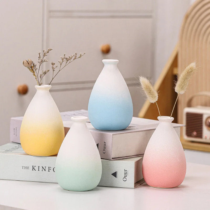 Four pastel gradient ceramic vases in pink, blue, yellow, and green arranged on books - RoomDen.