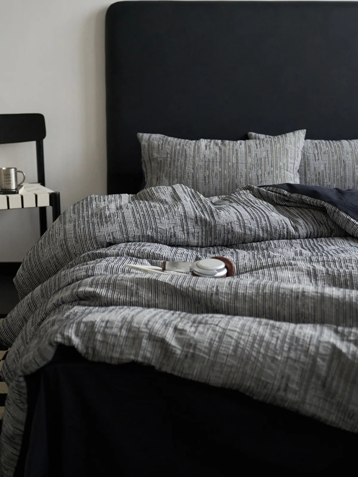Styled view of the Ash Grey pinstripe bedding with a black chair and metal cup nearby.