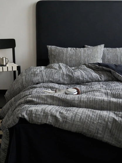 Styled view of the Ash Grey pinstripe bedding with a black chair and metal cup nearby.