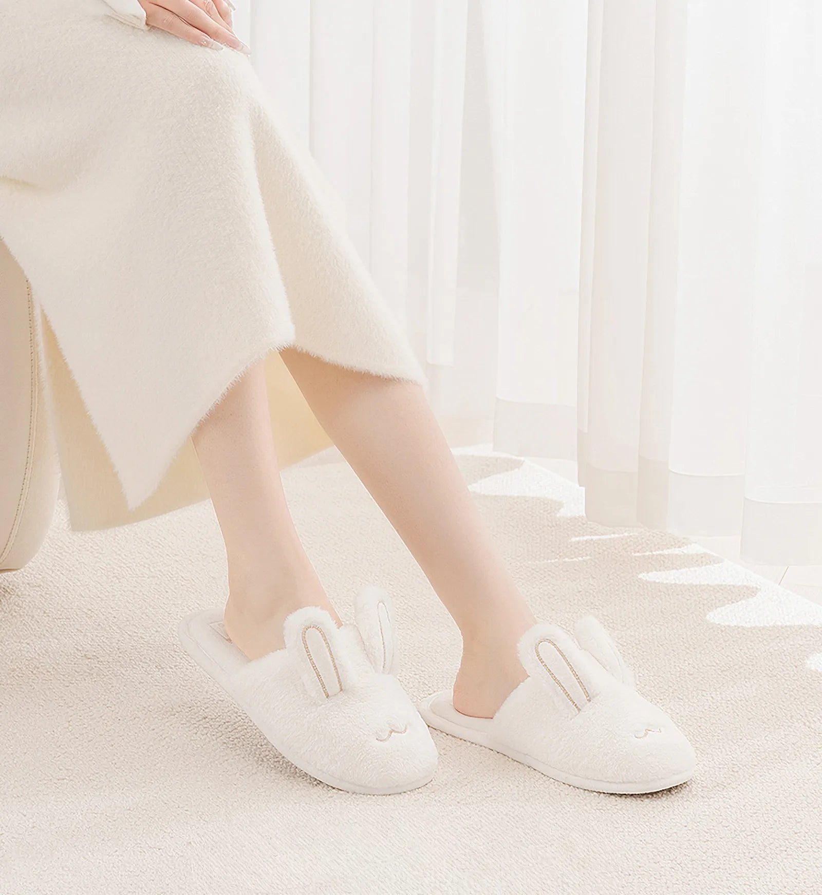 White plush bunny slippers on model legs in bright room - RoomDen