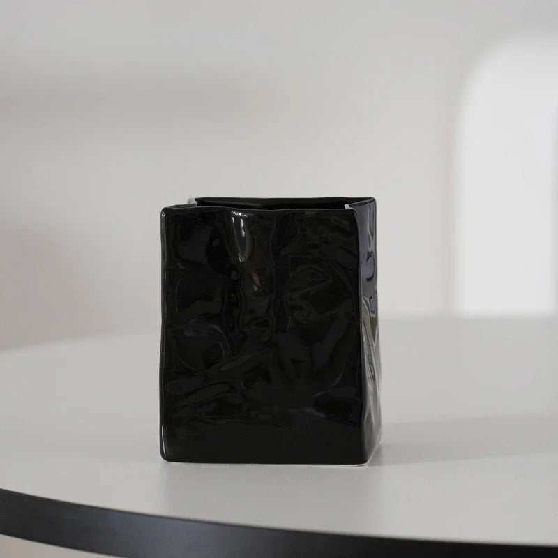 A single glossy black crumpled ceramic organizer on a white table with soft lighting. - RoomDen