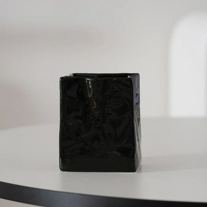 A single glossy black crumpled ceramic organizer on a white table with soft lighting. - RoomDen