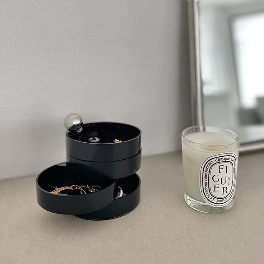 The Matte Black swivel jewelry organizer open on a neutral-toned desk next to a candle and mirror. - RoomDen