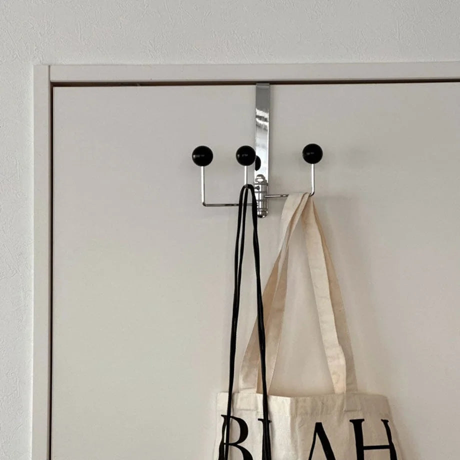 Main image of the black Smooth Ball Tip Metal Over-the-Door Hook hanging on a white door with a tote bag - RoomDen