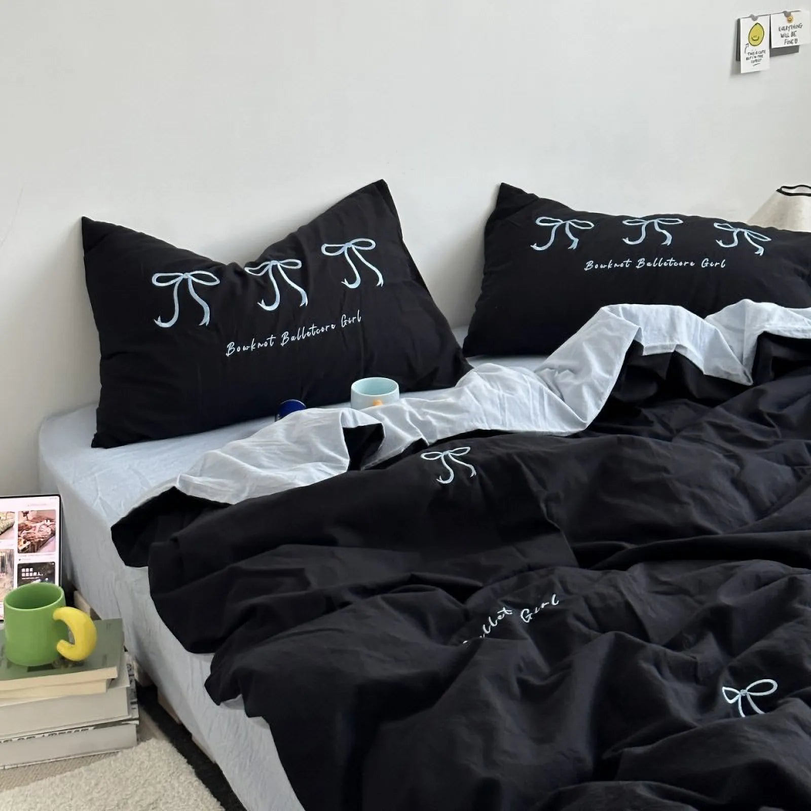 A black washed cotton bedding set with white embroidered bows, styled on a bed with a white sheet. - RoomDen