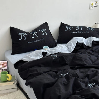 A black washed cotton bedding set with white embroidered bows, styled on a bed with a white sheet. - RoomDen