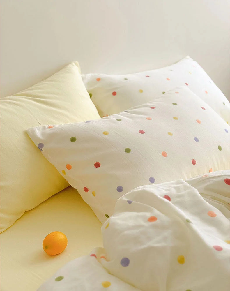 Polka dot pillowcase next to a solid yellow pillow with a small orange resting on the bed - RoomDen
