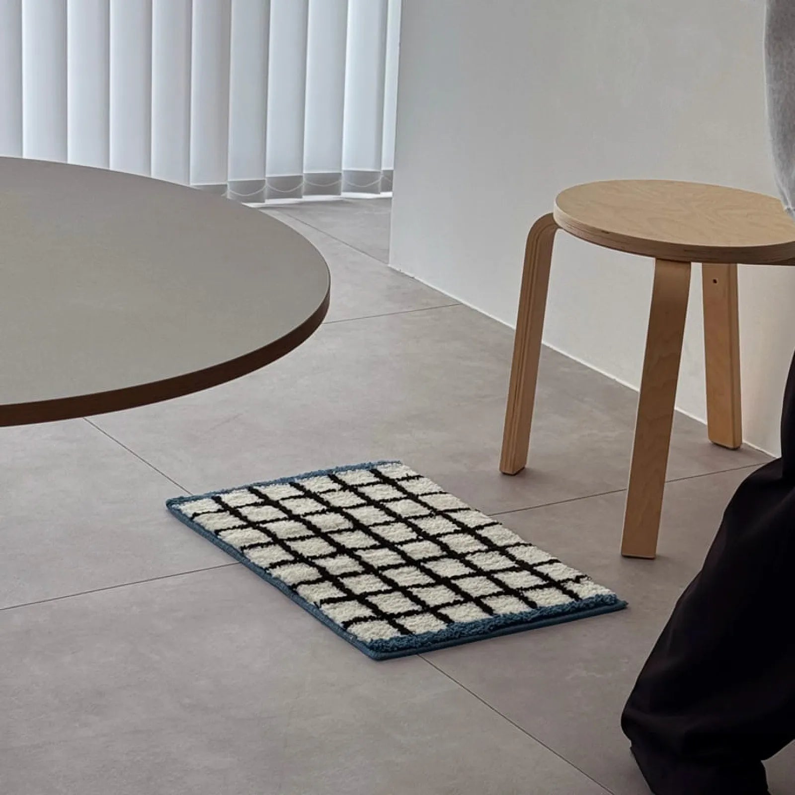 White and blue checkered accent rug displayed on a grey tile floor next to a wooden stool - RoomDen