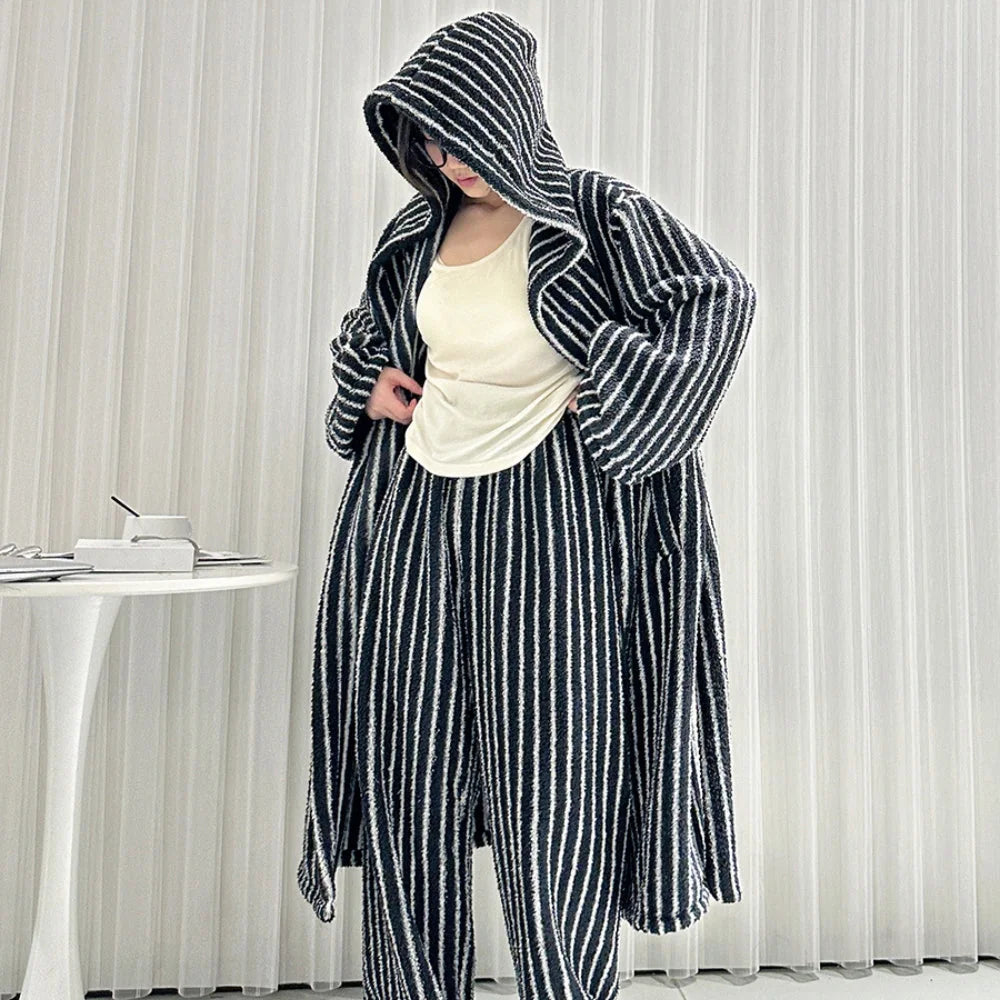 Model adjusting the top under her black and white striped hooded robe, showing the relaxed fit of the pajama set - RoomDen.