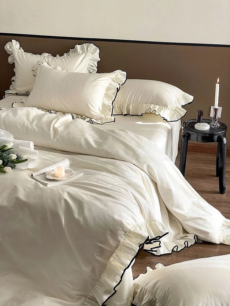 Angled shot of the Cream White ruffled bedding set, showing the silky Tencel fabric and a candle on a side table - RoomDen.