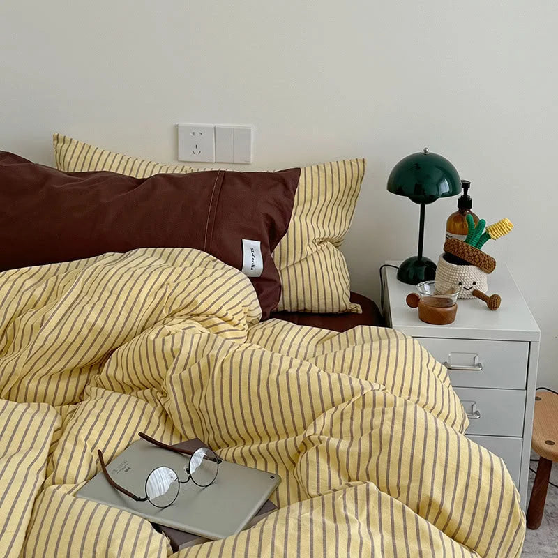 Full view of the bed with the Yellow & Brown Striped Bedding Set, showing a solid brown pillow and glasses on a laptop - RoomDen.